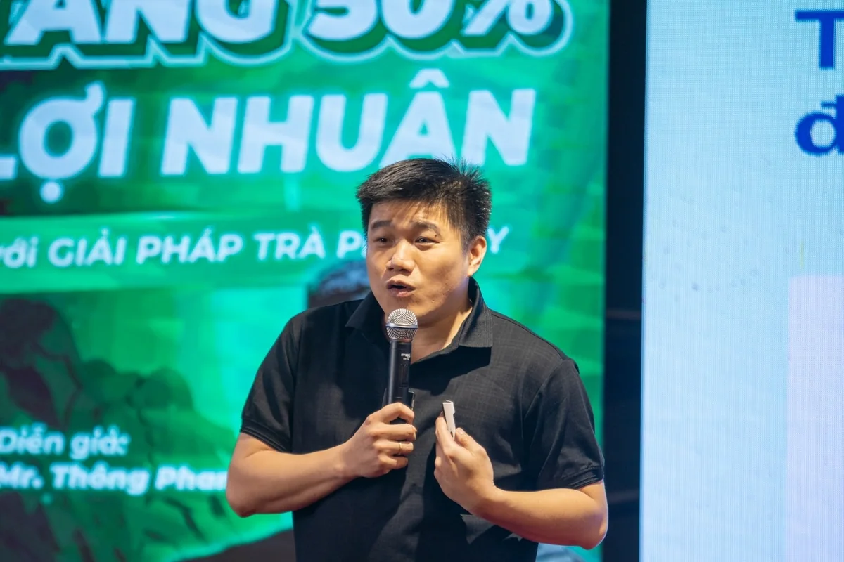 Thông Phan cầm micro chia sẻ trên sân khấu tại một sự kiện kinh doanh.